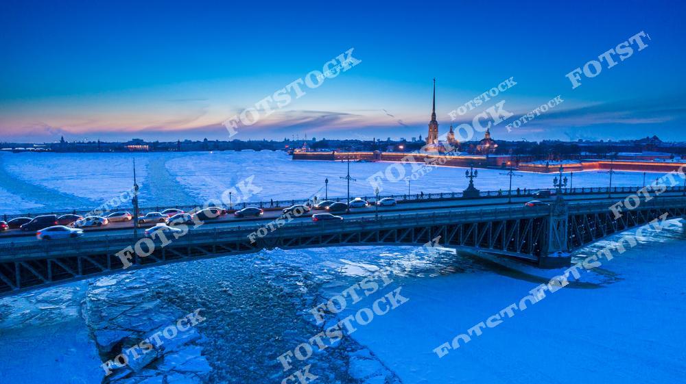 Панорамная фотография зимнего Санкт-Петербурга с высоты птичьего полета. На снимке видны Троицкий мост через Неву, ледяная поверхность реки и Петропавловская крепость, символ исторического центра города. Снимок подчеркивает красоту зимнего Петербурга, архитектуру мостов и крепости, а также атмосферу снежного города. Вид с дрона позволяет увидеть масштабы городской застройки и природно-архитектурное окружение Невы в зимнее время. Фотография подходит для туристических публикаций, фотостоков, оформления интерьеров, рекламы и иллюстраций о зимнем Петербурге и его достопримечательностях.